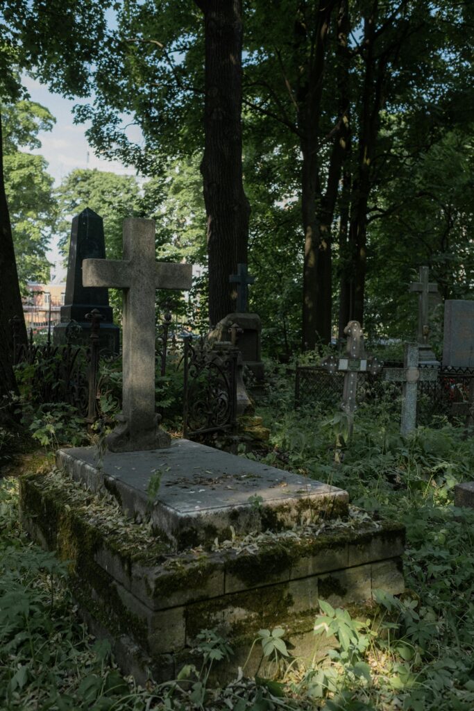 Peaceful cemetery with moss-covered tombstone and cross in nature surroundings.
